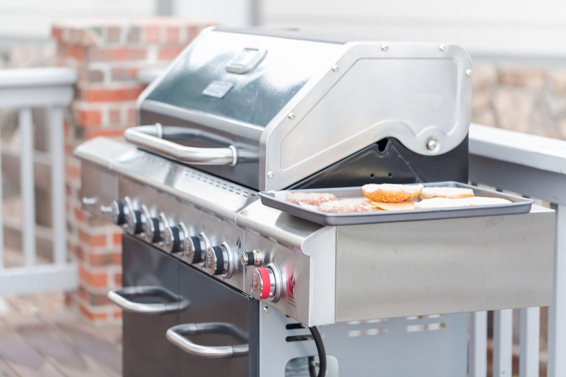 A grill with a tray of food on it is on a deck.