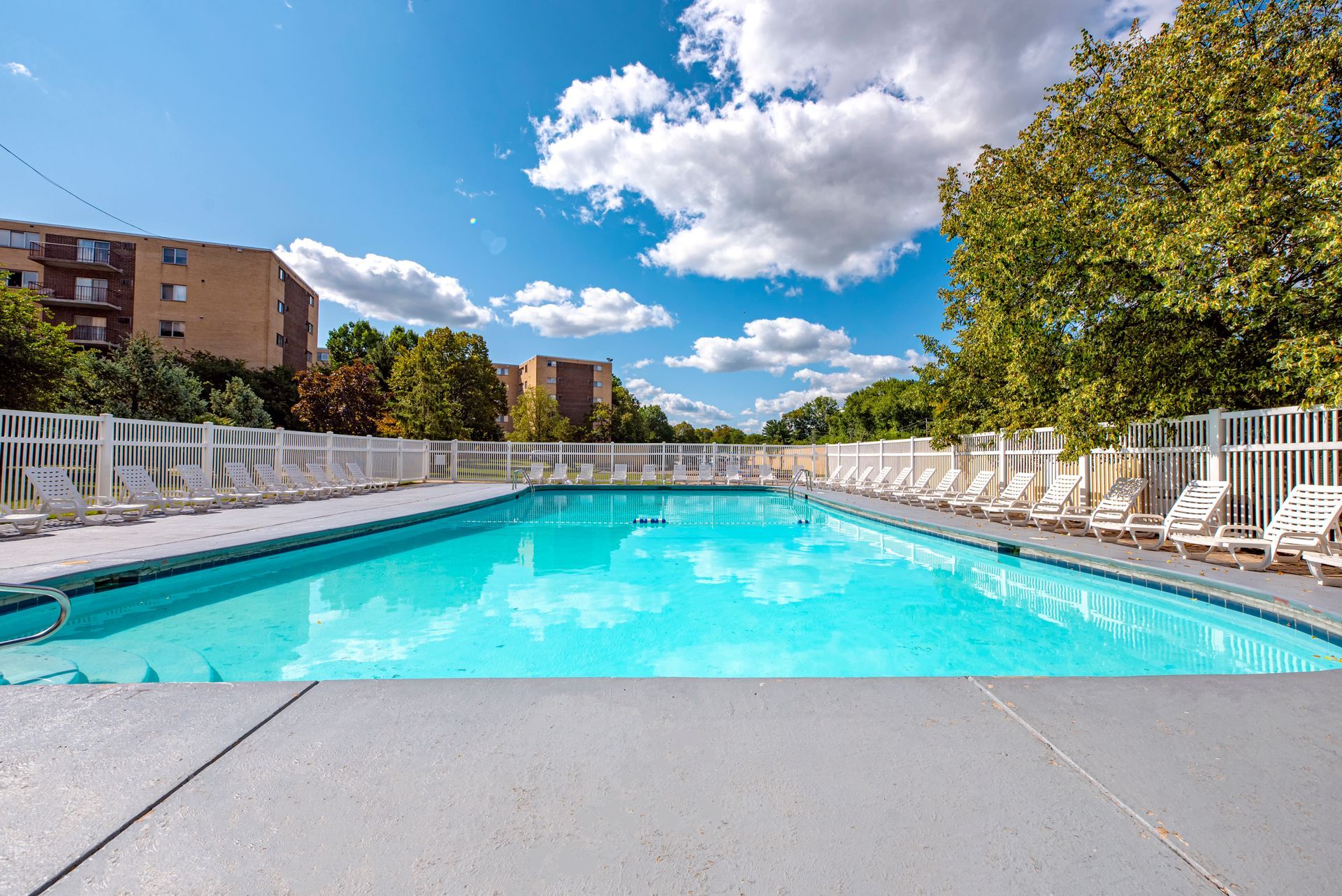 A large swimming pool surrounded by chairs and trees on a sunny day.