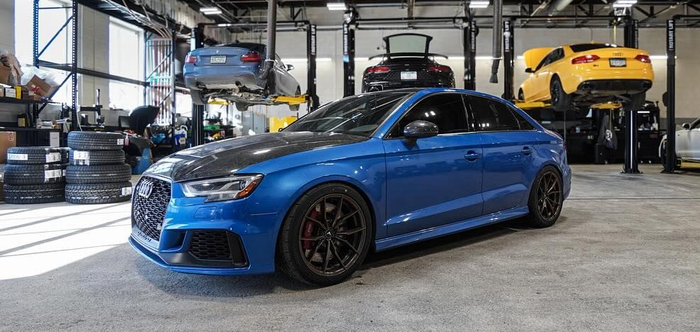 Blue car in a repair shop with other cars on lifts.