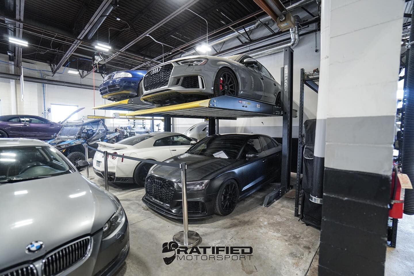 Cars in a garage, several on lifts, including an Audi and BMW.