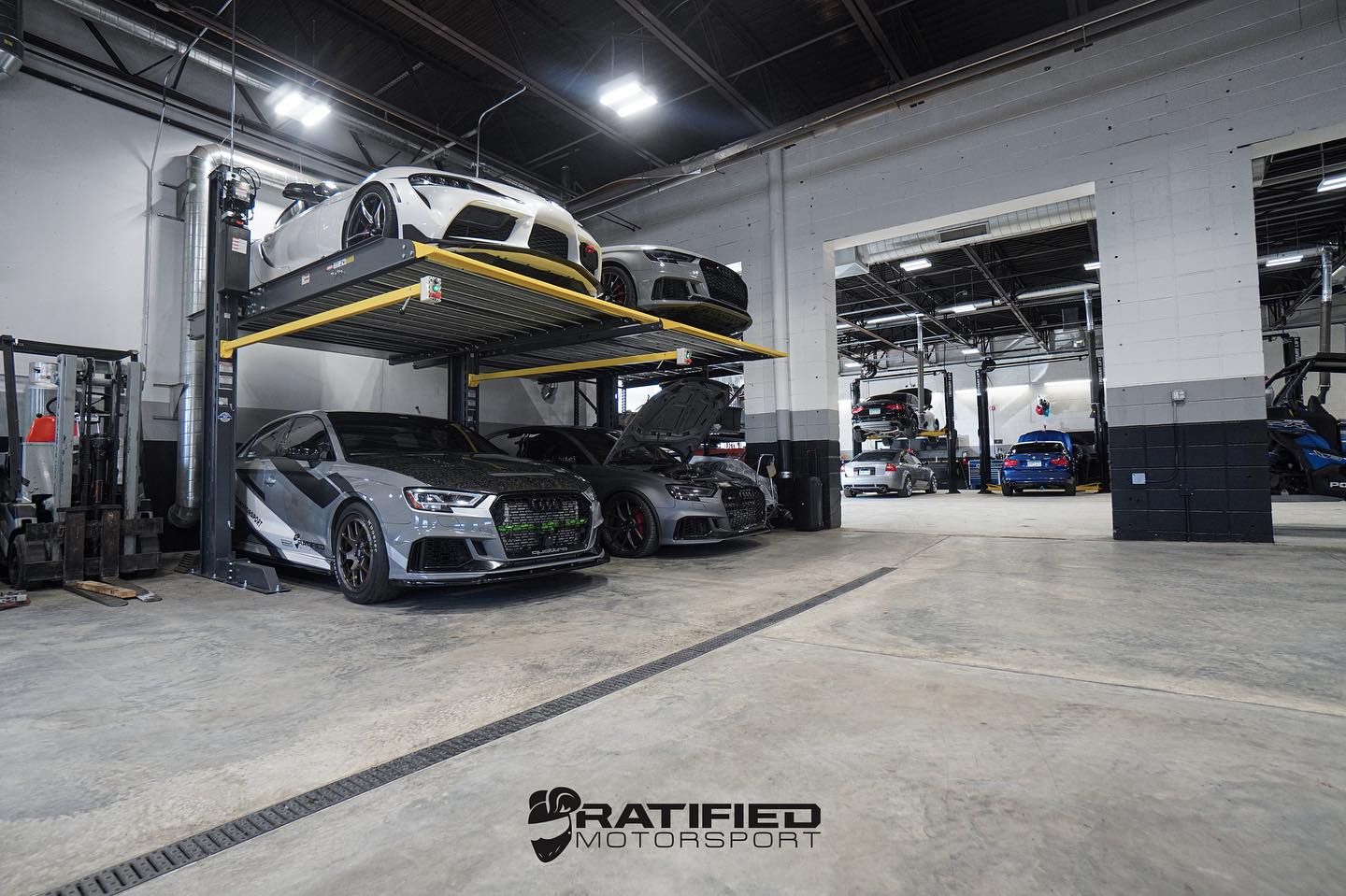 A multi-level car lift holding multiple cars in a brightly lit auto shop.