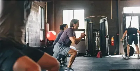 People exercising at Strive Fitness gym in South Jordan, UT, with some squatting while others use exercise machines.