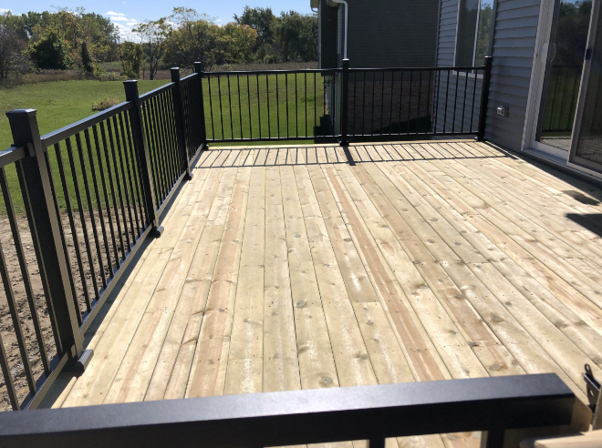 A wooden deck with a black railing and a house in the background.