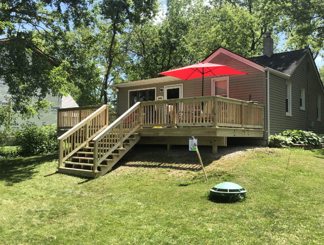 A house with a large deck and stairs and a red umbrella.