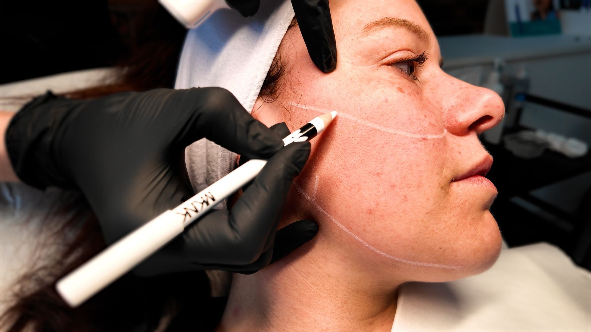 A person is drawing a line on a woman 's face with a marker.