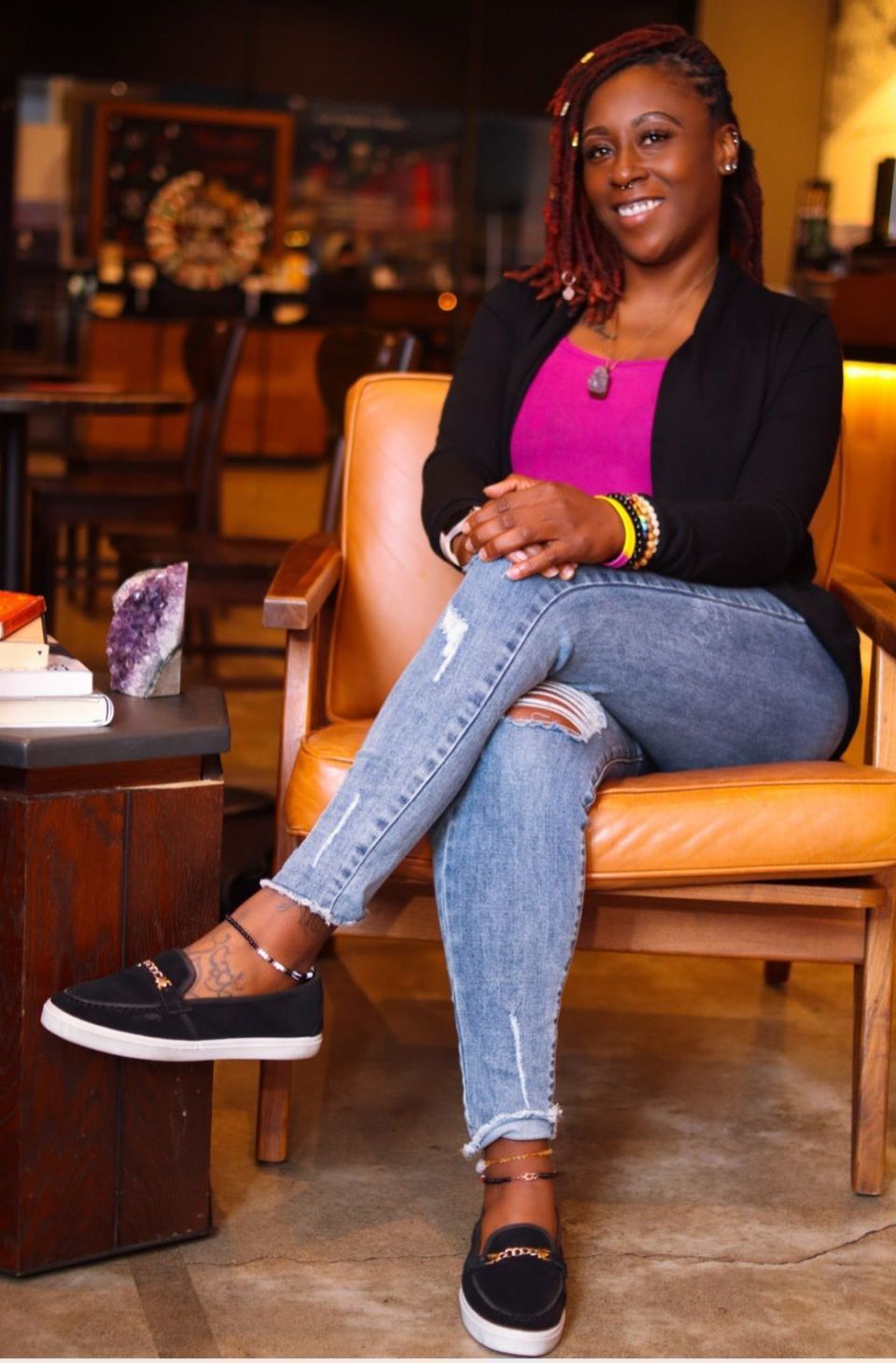 Professional photo of Alexandrea Long, LCSW-S, Black woman trauma therapist sitting casually in office chair, smiling warmly at camera in business casual attire