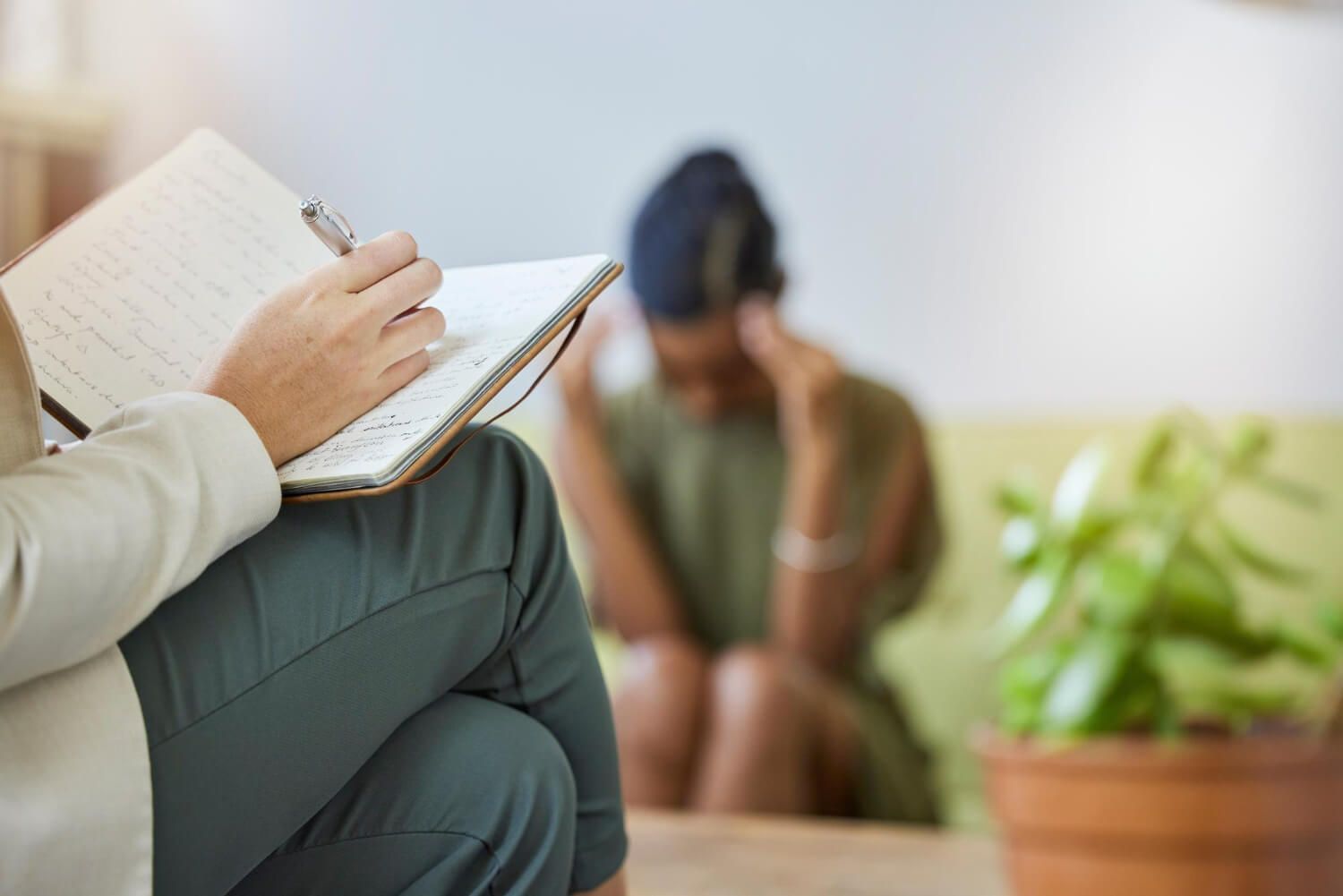 Professional therapist taking notes during IFS therapy session while client processes trauma in safe therapeutic environment