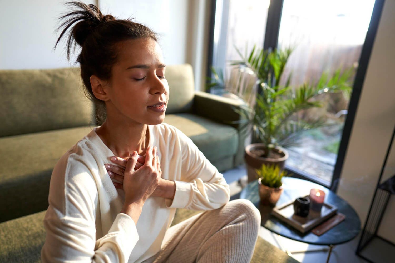 Woman in white top sitting peacefully with eyes closed practicing breathing exercises for nervous system regulation at home
