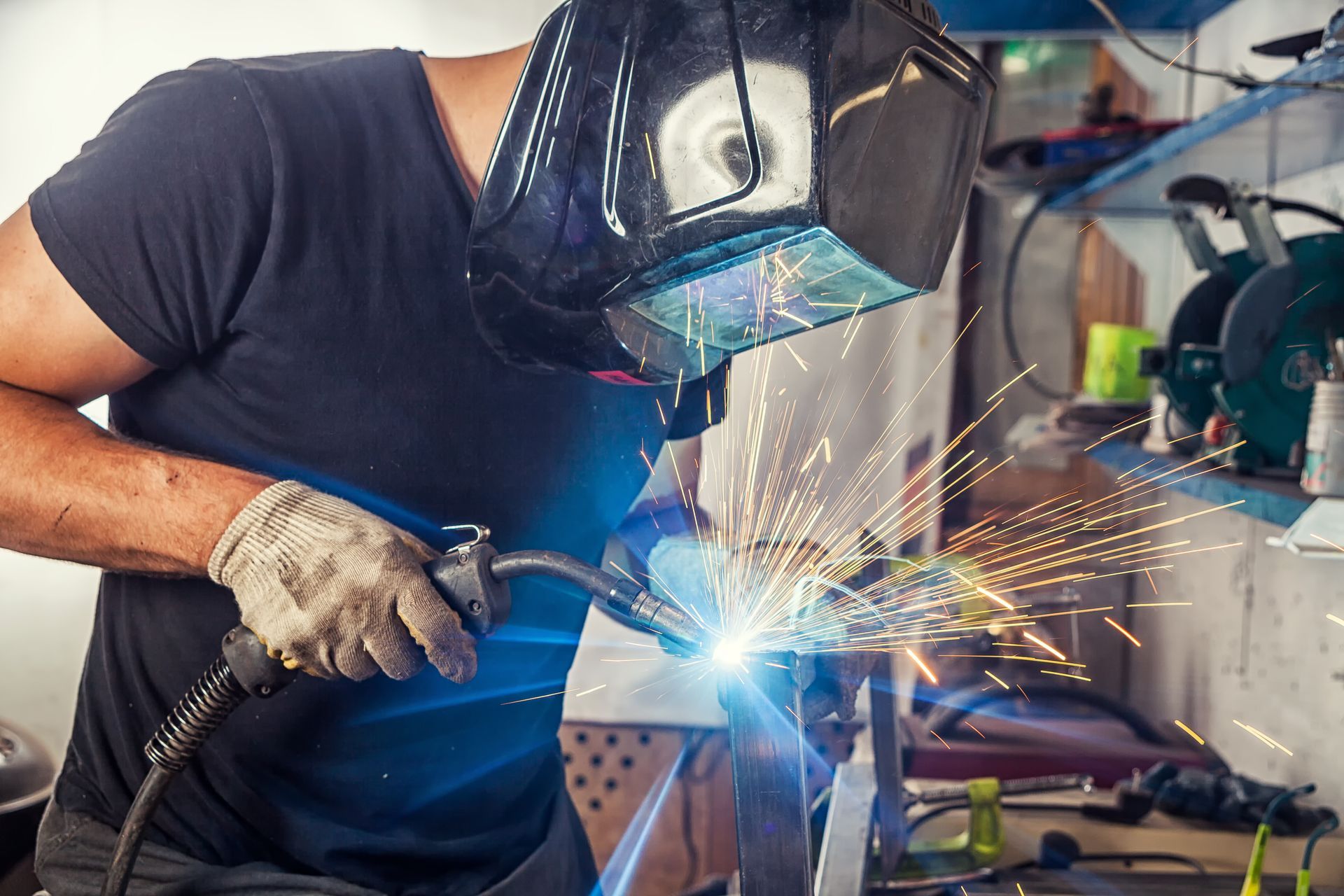 Welder wearing a dark helmet, welding metal. Sparks fly in a workshop setting.