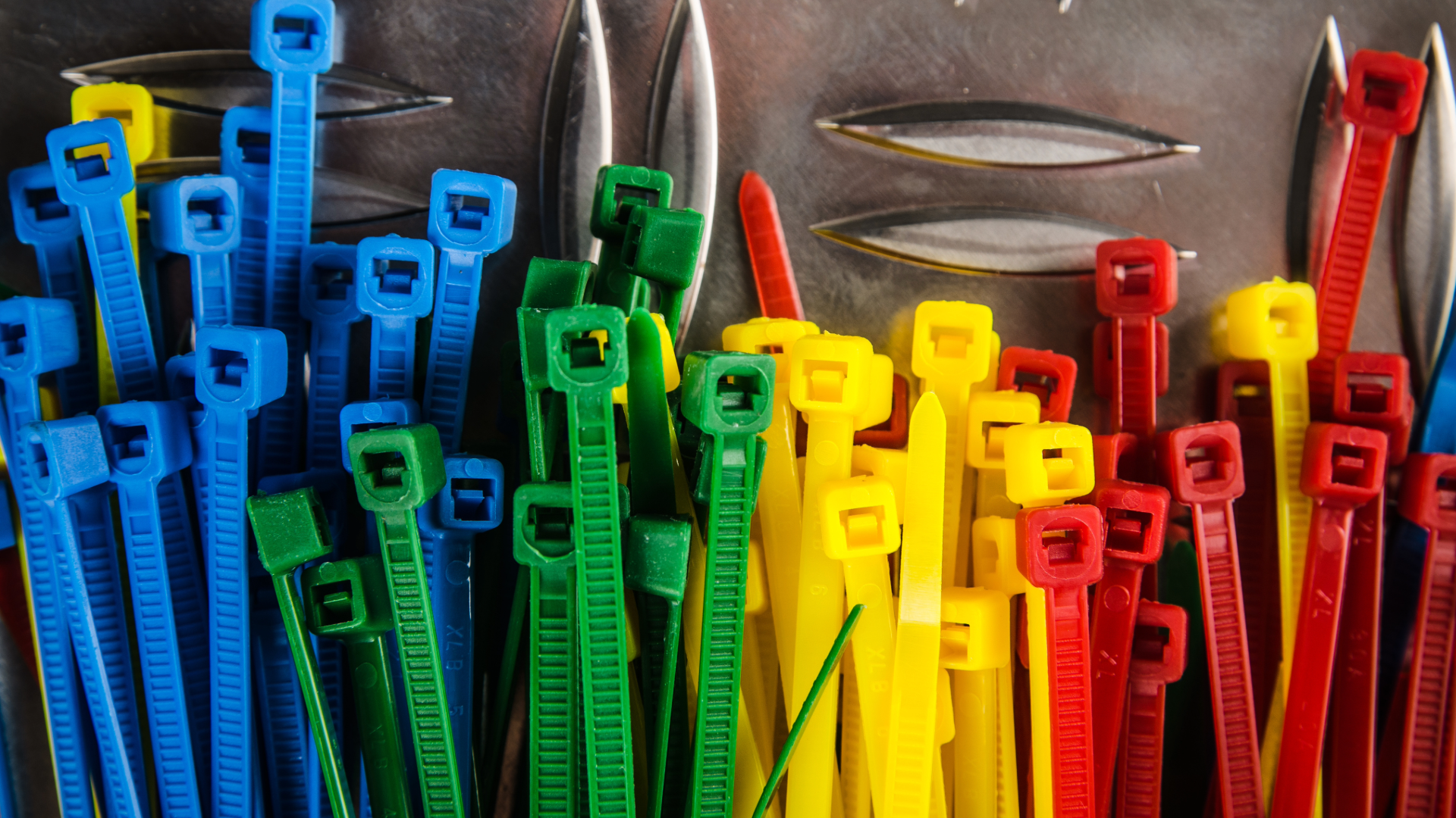 A collection of colorful plastic zip ties, including blue, green, yellow, and red, arranged vertically on a metallic surface.