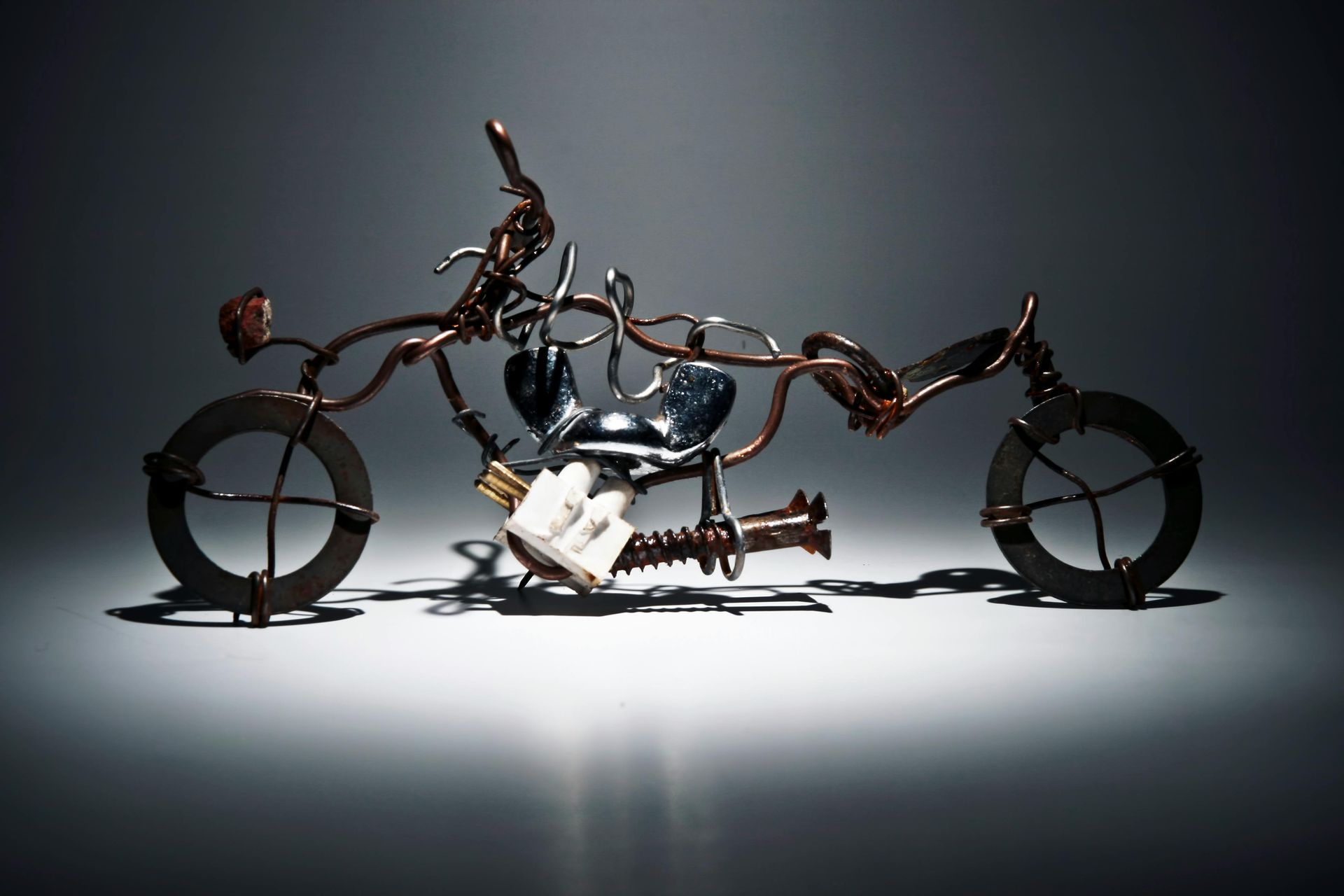 Sculptural motorcycle made of wires and metal parts, set against a dark, lit background.