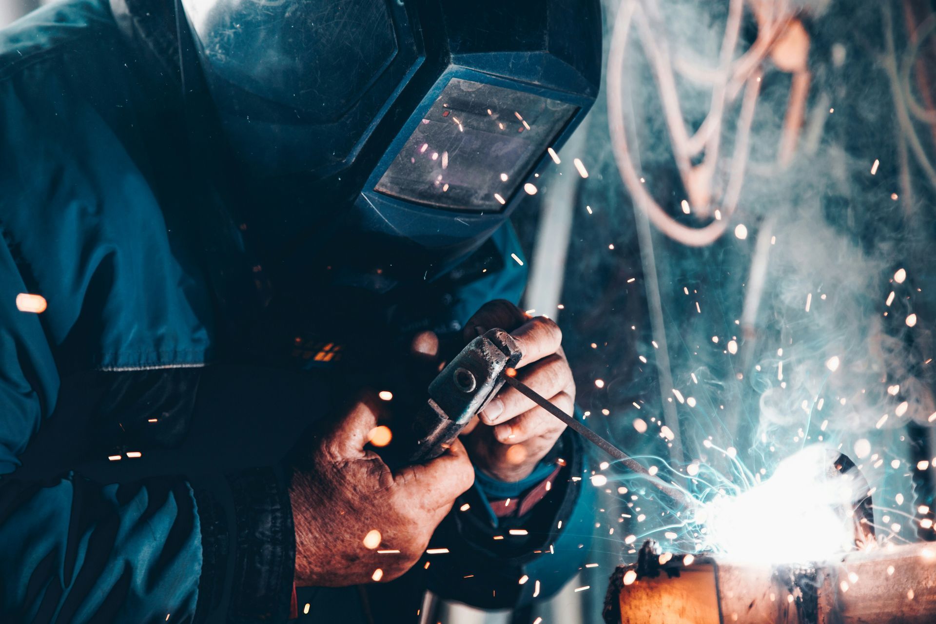 Welder in blue work clothes, welding metal with sparks flying, in an industrial setting.