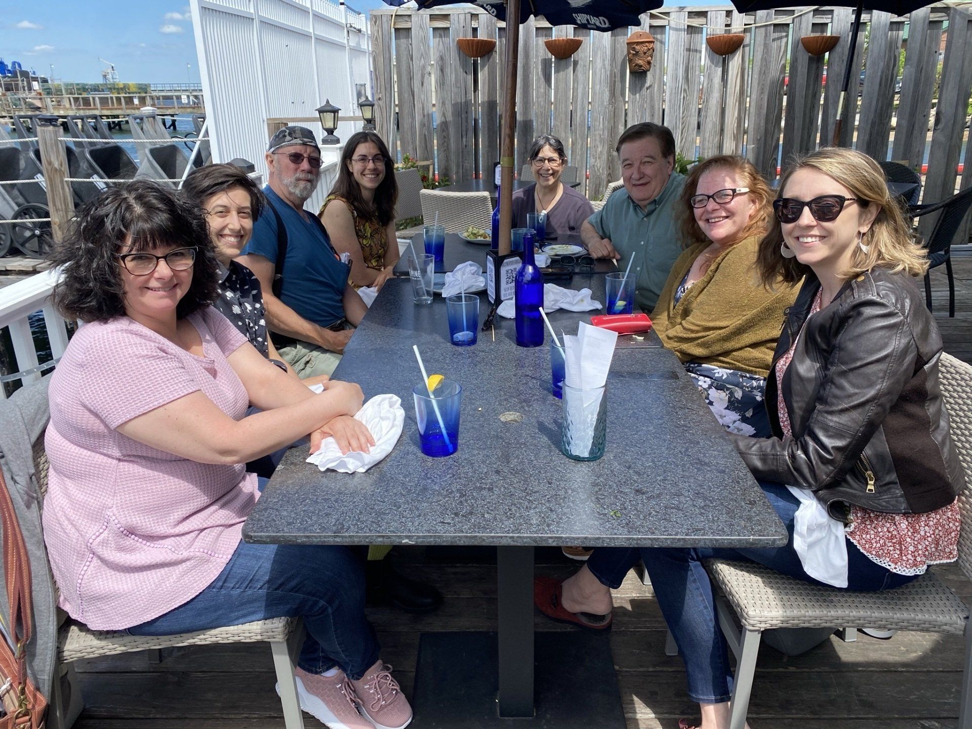 A group shot of TBE's eight staff members out at lunch - Sherri (a white woman with shoulder length dark hair and glasses); Zoe (a white person with short dark hair); Bob (a white man with a grey beard and sunglasses); Abby (a white woman with long brown hair and glasses); Rabbi Braun (a white woman with dark hair pulled back and glasses); Dave (a white man with short brown hair); Deb (a white woman with long red hair and glasses); and Kate (a white woman with blonde shoulder length hair and sunglasses)
