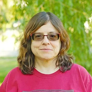 Headshot of Sandrea Kornblum, a white woman with shoulder length brown hair and pink, progressive glasses. She is wearing a magenta shirt.