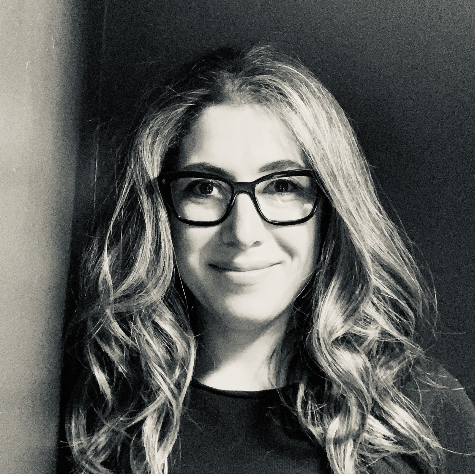 Black and white headshot of Lauren Fridling, a white woman with long wavy hair and black rectangular glasses. She is wearing a black shirt.