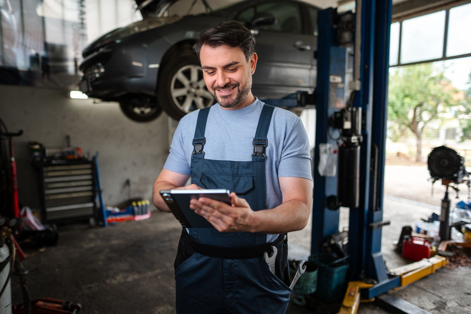 Mechanic using a tablet while working in an auto repair shop with a car on a lift. Mechanic using a tablet while working in an auto repair shop with a car on a lift.