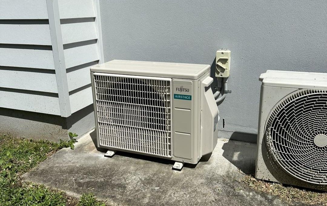 Two beige residential outdoor air conditioning units mounted on a concrete pad against a house wall.