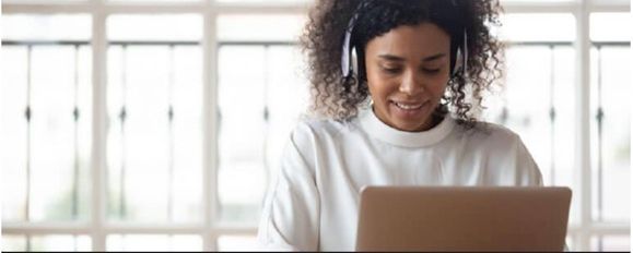 A woman wearing headphones is using a laptop computer.