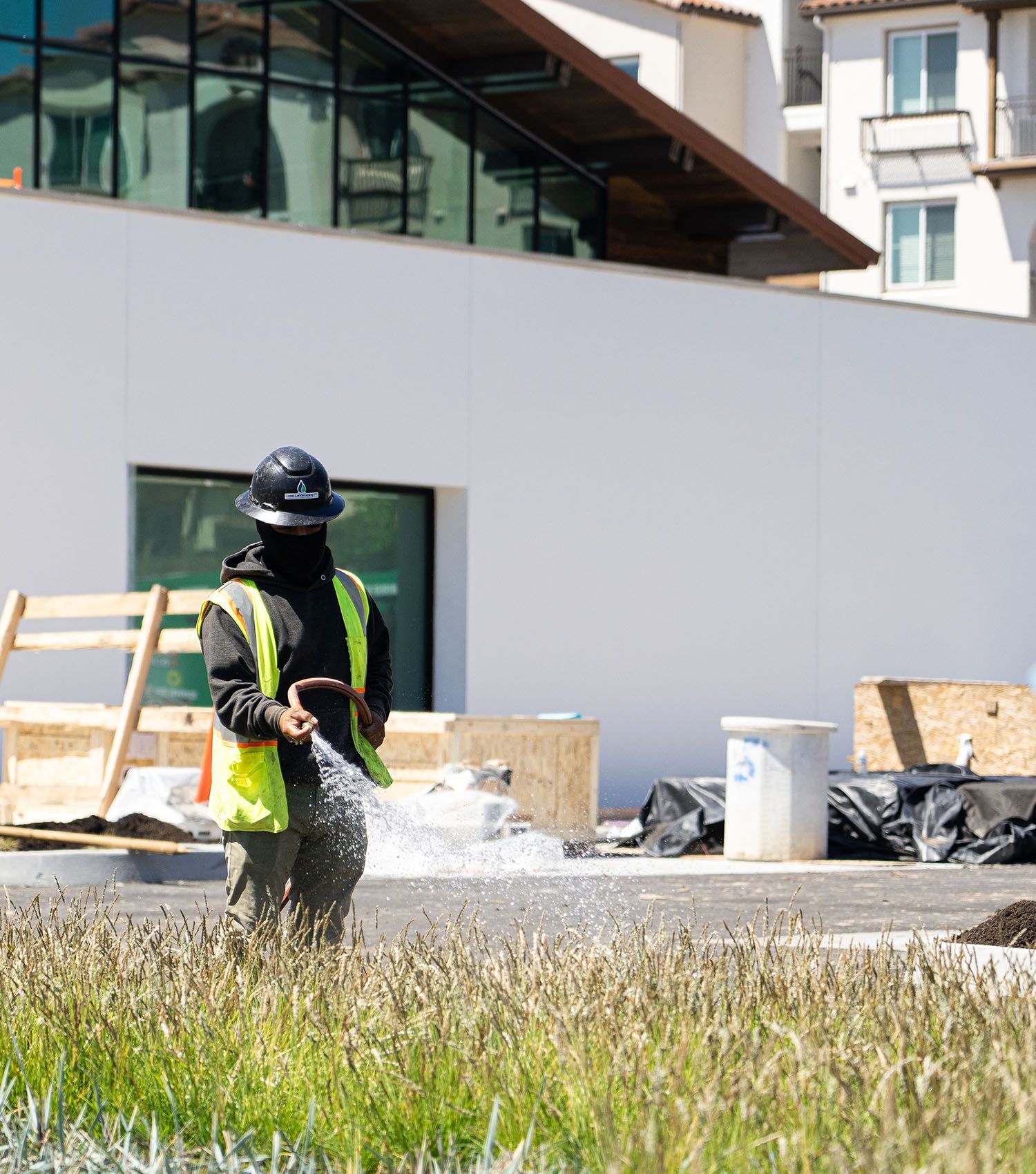 A man wearing a hard hat and safety vest is spraying grass