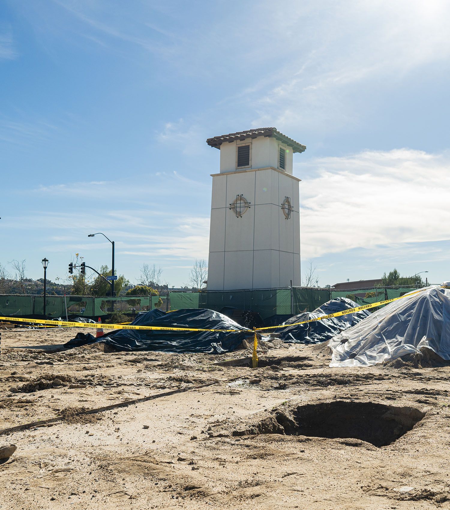 A large white clock tower is sitting in the middle of a dirt field.