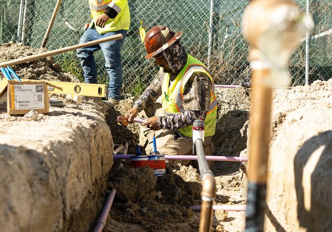 Two construction workers are working on a pipe in the dirt.