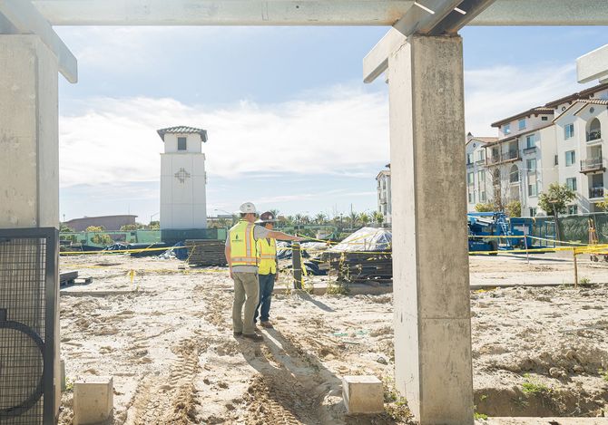 Two construction workers are standing on a construction site looking at a building under construction.