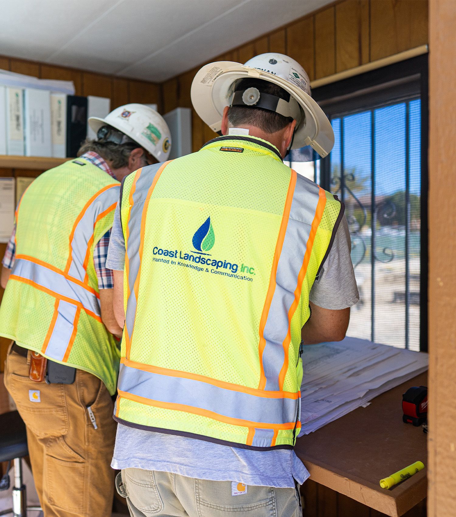 Two construction workers wearing safety vests and hard hats