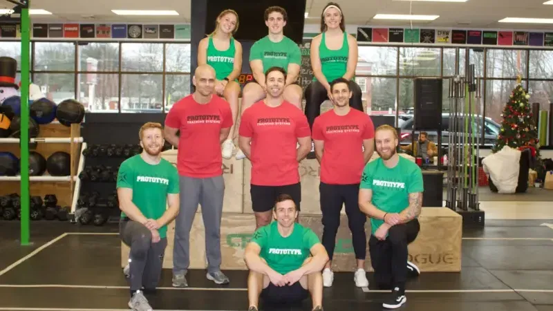 A young boy wearing a green shirt with a shamrock on it is flexing his muscles in a gym.