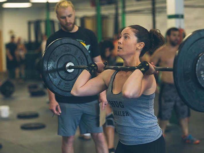 A woman is lifting a barbell over her head in a gym.