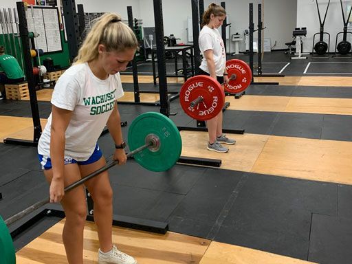 A woman in a white shirt is lifting a barbell in a gym.