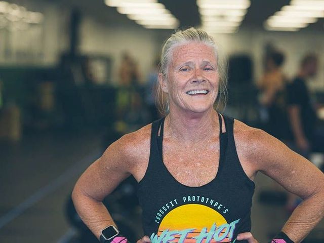 A woman in a black tank top is smiling in a gym.