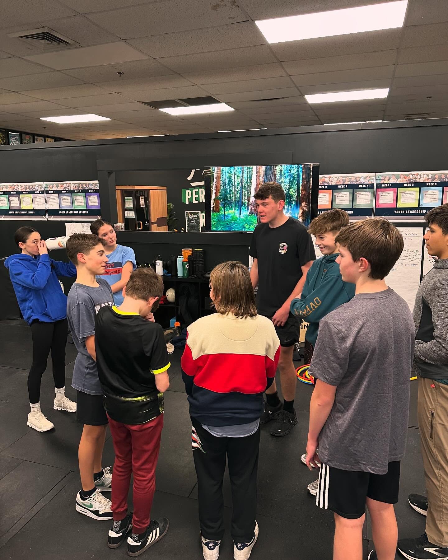 A young boy wearing a green shirt with a shamrock on it is flexing his muscles in a gym.
