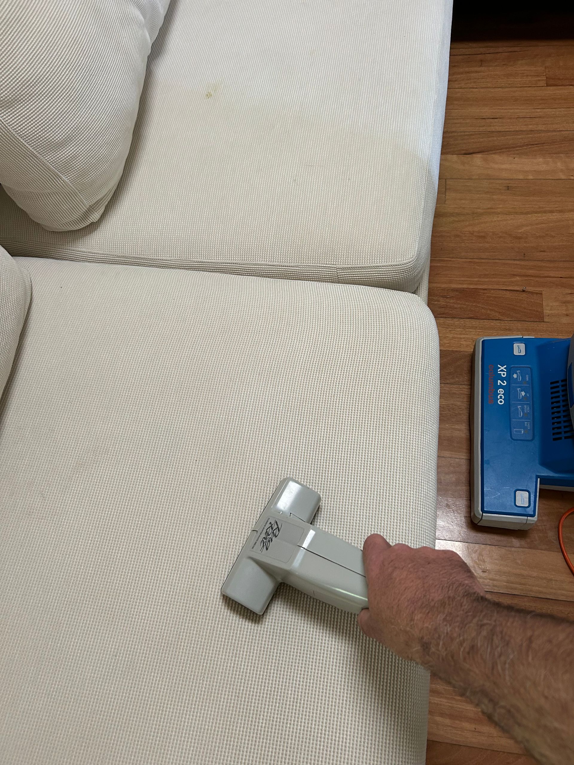 A Person is Cleaning a Couch With a Vacuum Cleaner — Rugrats Carpet Cleaning Service In Tuncurry, NSW