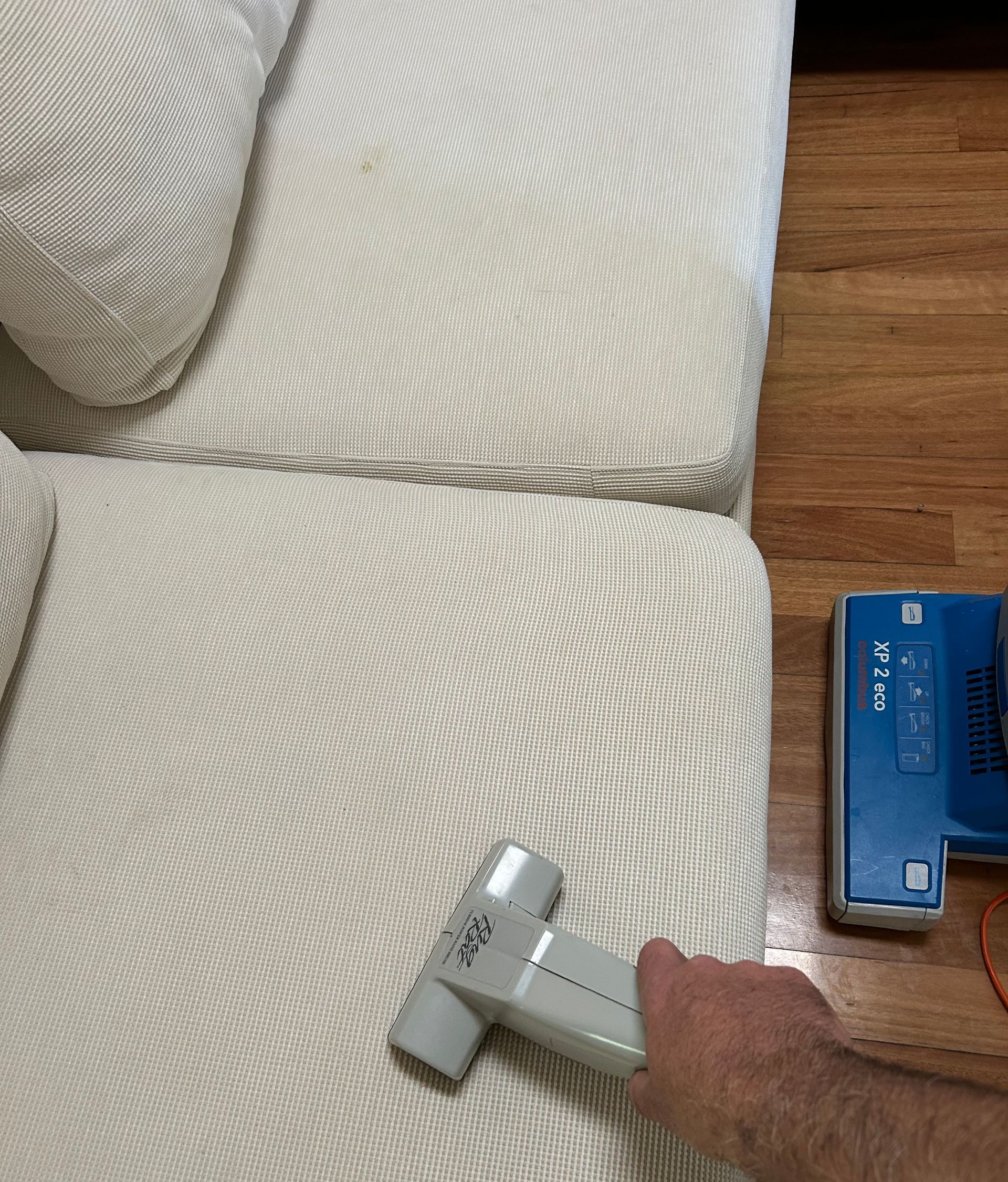 A Person is Cleaning a Couch With a Vacuum Cleaner — Rugrats Carpet Cleaning Service In Charlotte Bay, NSW