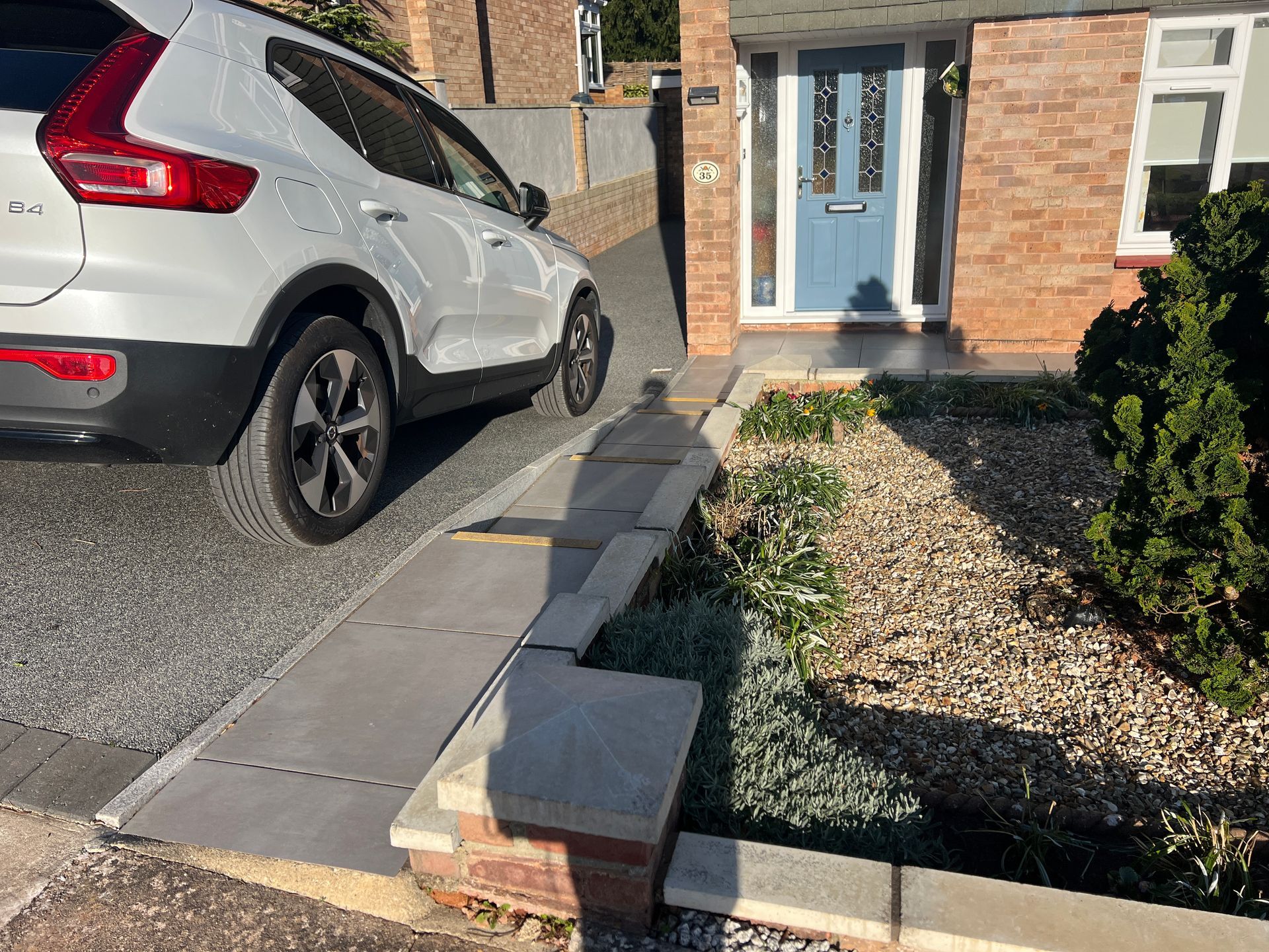 Grey resin driveway with a white car on it, in front of a red brick home.