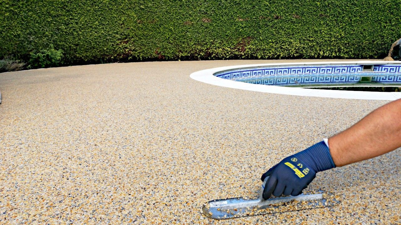 Resin being smoothed over surface next to a swimming pool.