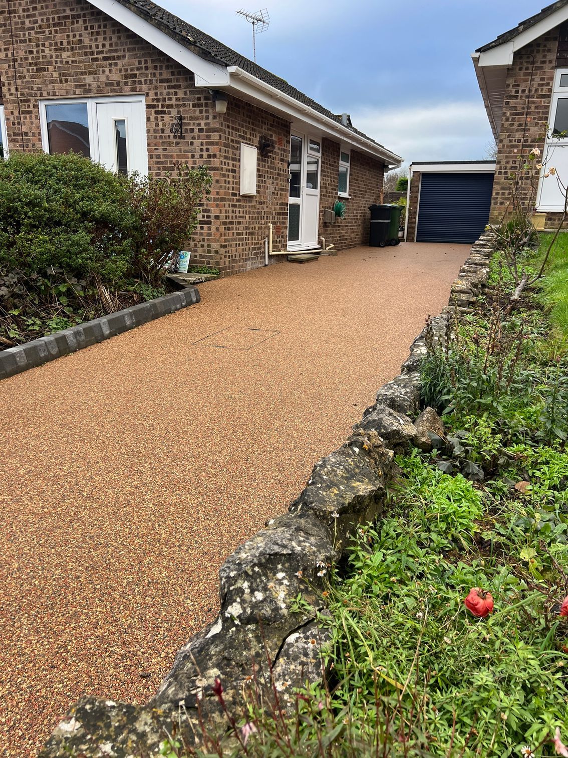 Brown resin driveway outside a row of bungalows, surrounded by a stone wall border.
