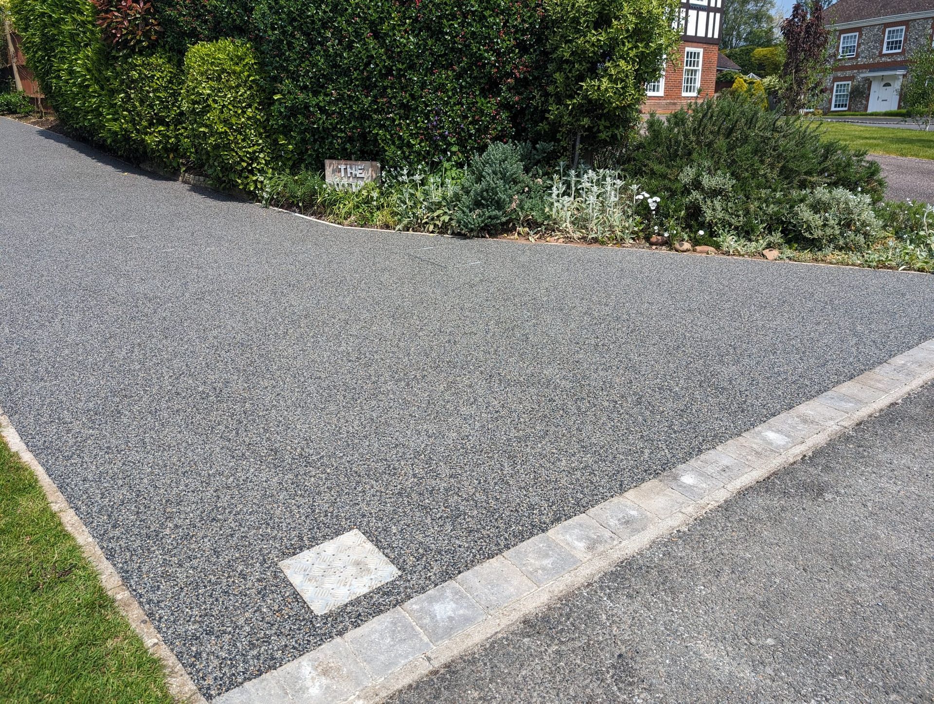 Dark grey resin driveway with a light block border and a small manhole cover.