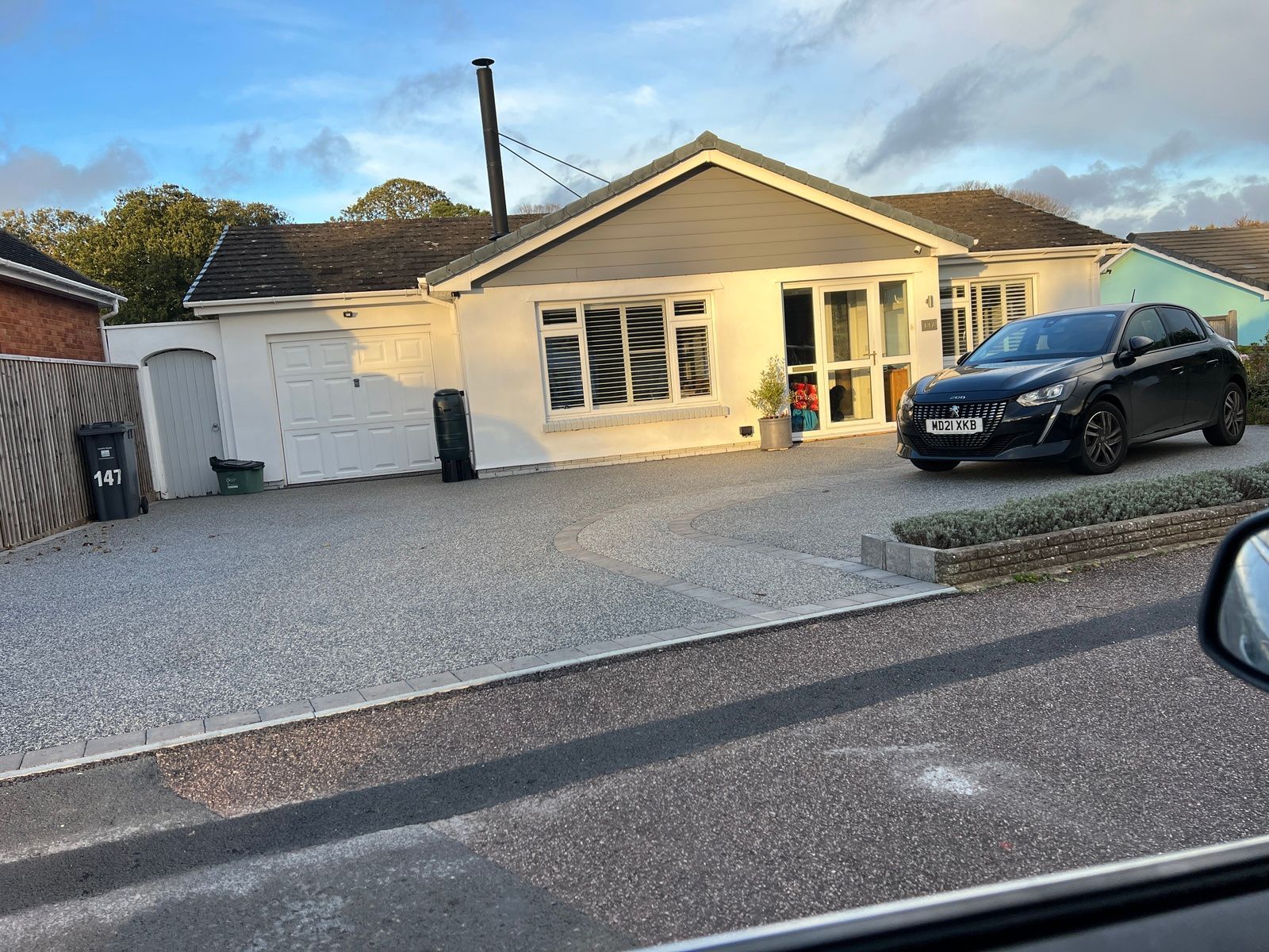Grey resin driveway outside a white bungalow. There is a black car parked on the right-hand side