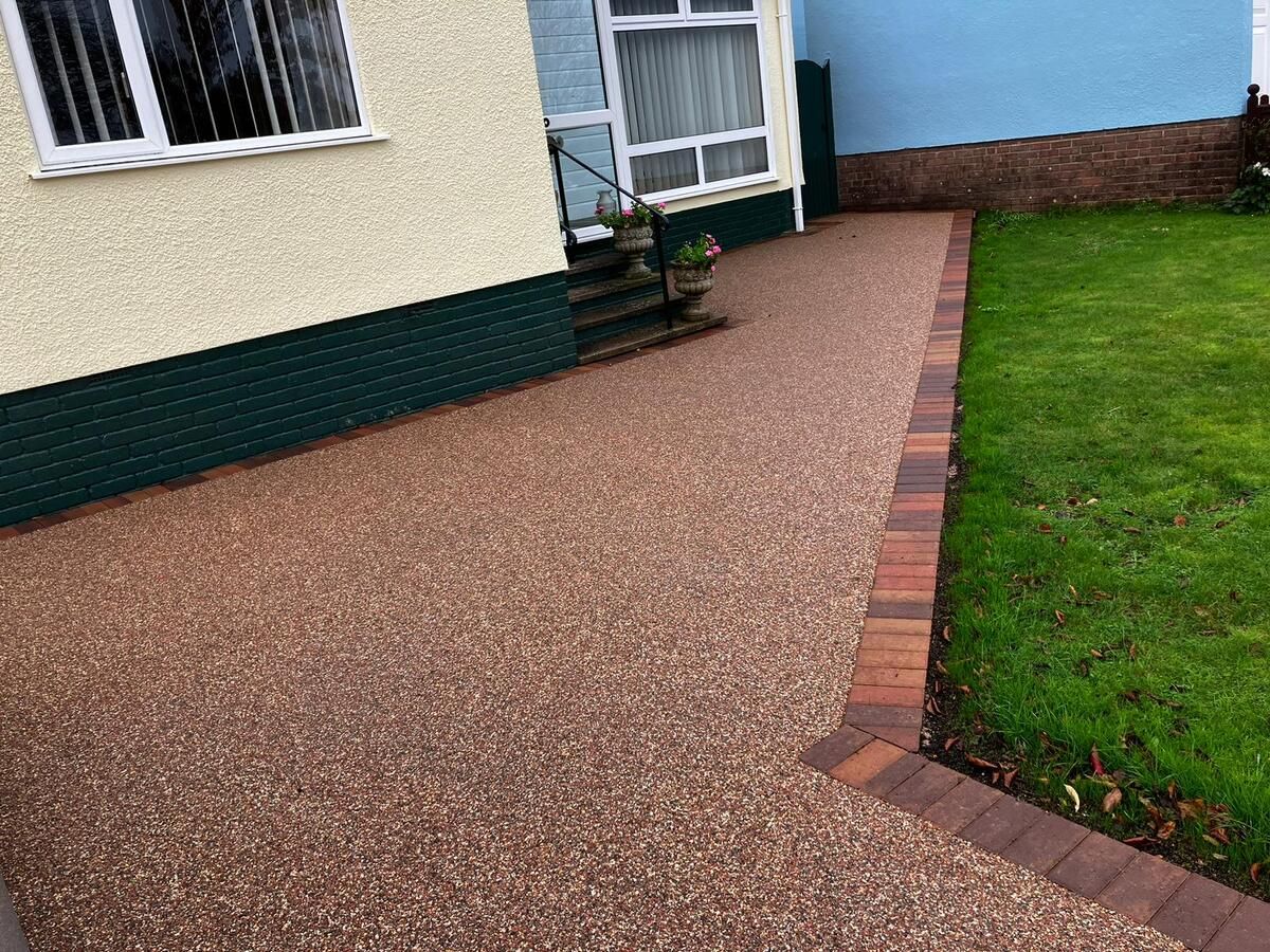 Red resin pathway with orange, brown, and red block paving border, with grass on the side.