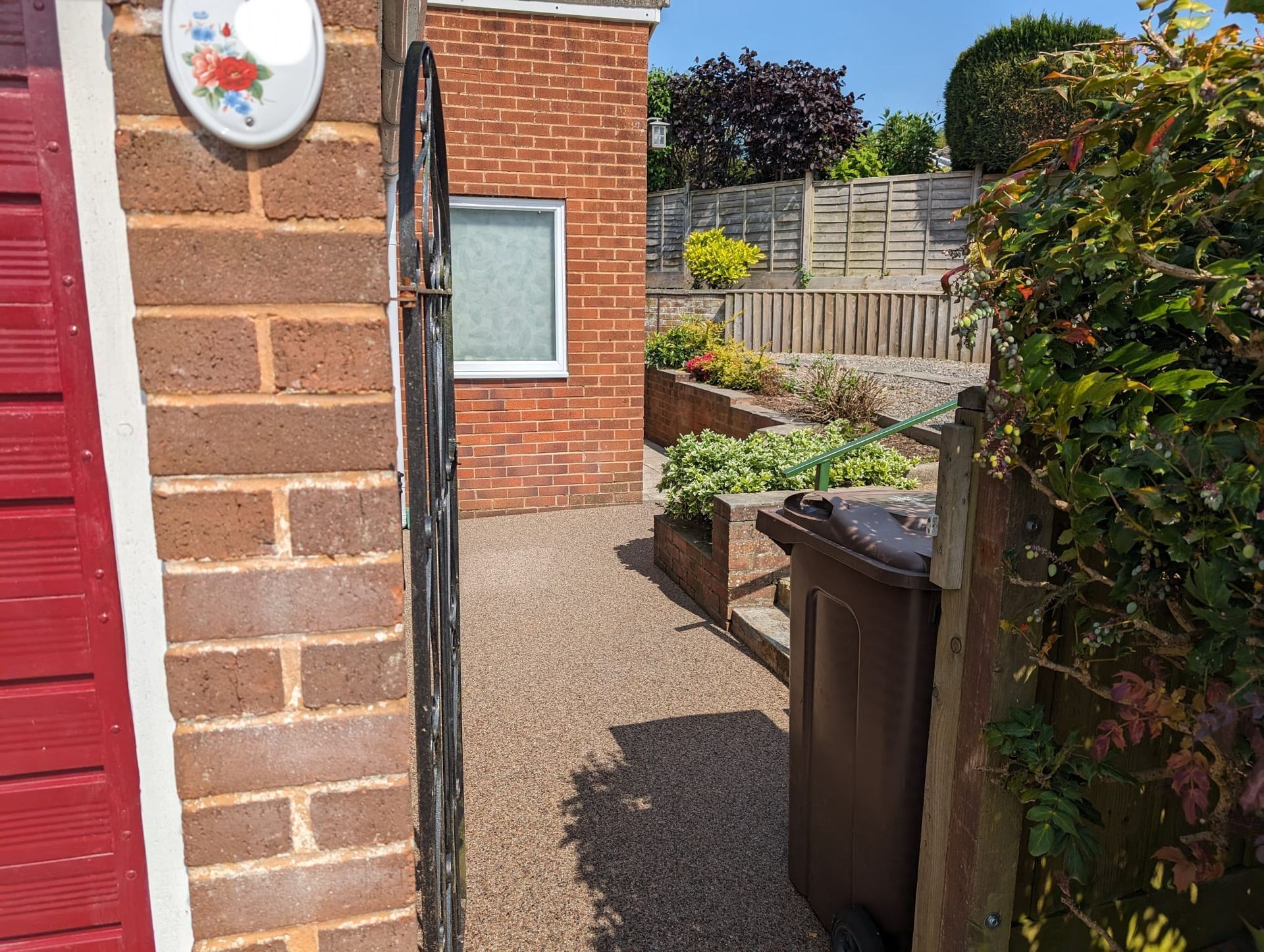 Red resin pathway with orange, brown, and red block paving border, with grass on the side.