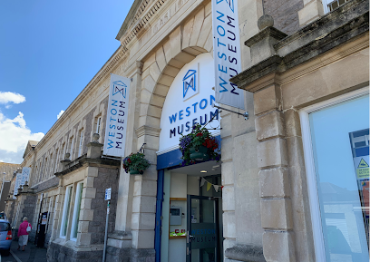 Weston Museum entrance with blue banners, stone facade, and flower baskets.