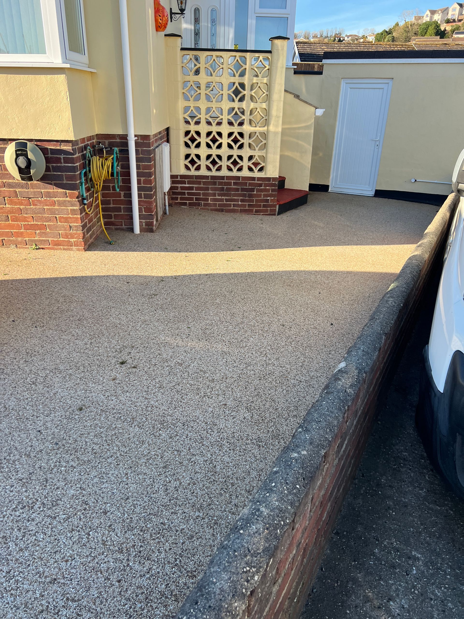 A car is parked in front of a house next to a brick wall.