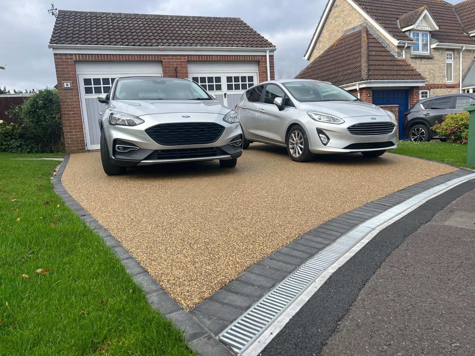 Two cars are parked in a driveway in front of a house.