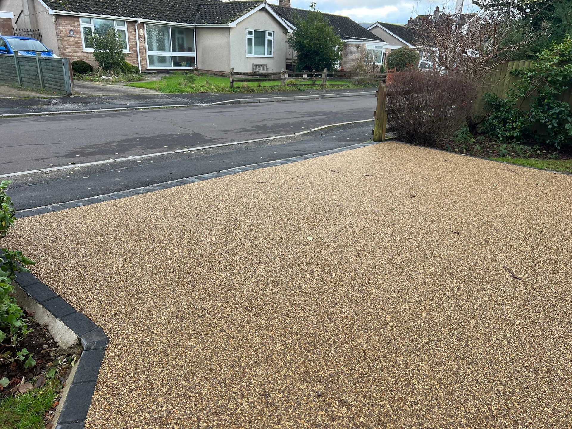 A gravel driveway next to a road with a house in the background.