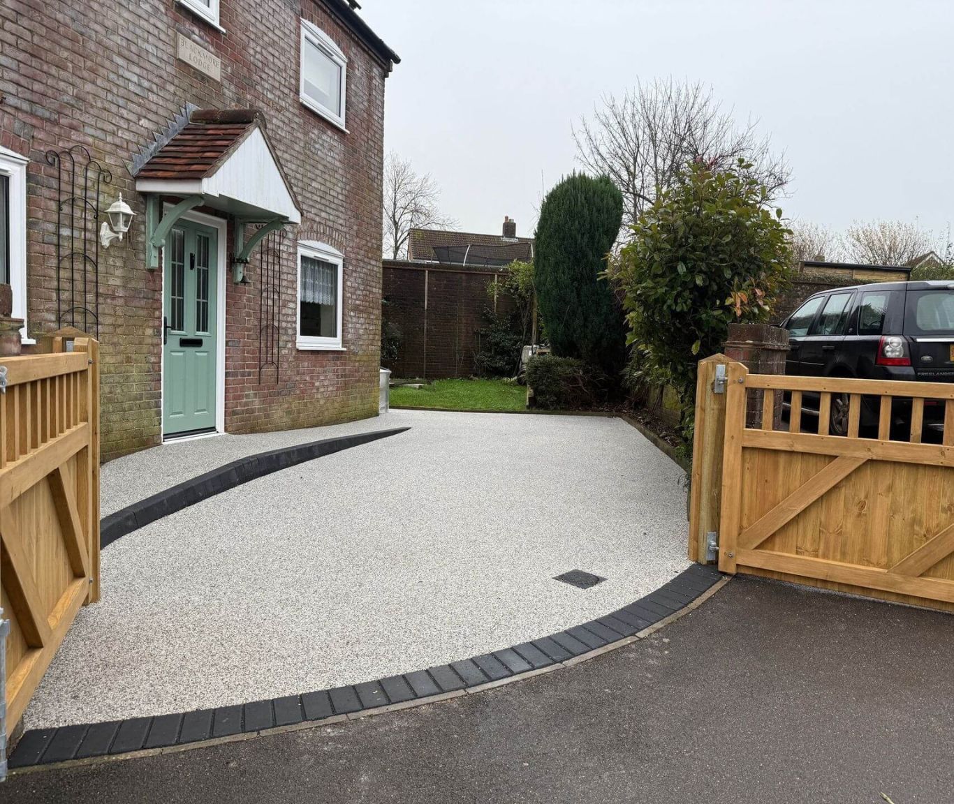 A car is parked in front of a house with a wooden gate.