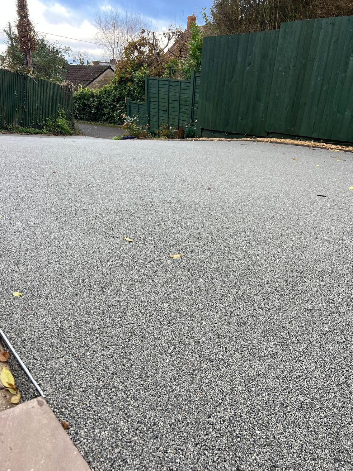 A gravel driveway with a green fence in the background.