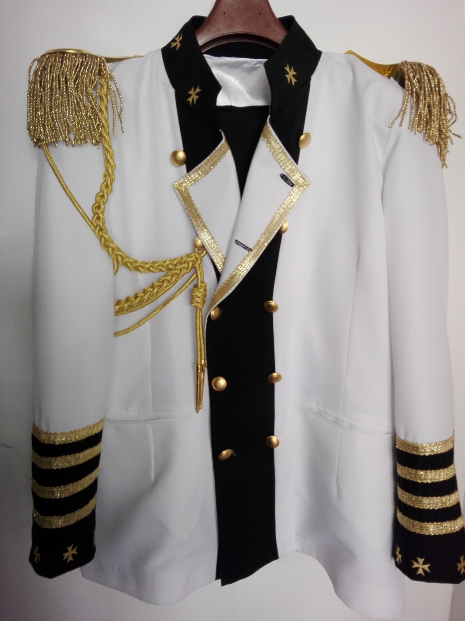 Una giacca bianca e nera con finiture dorate è appesa a una gruccia