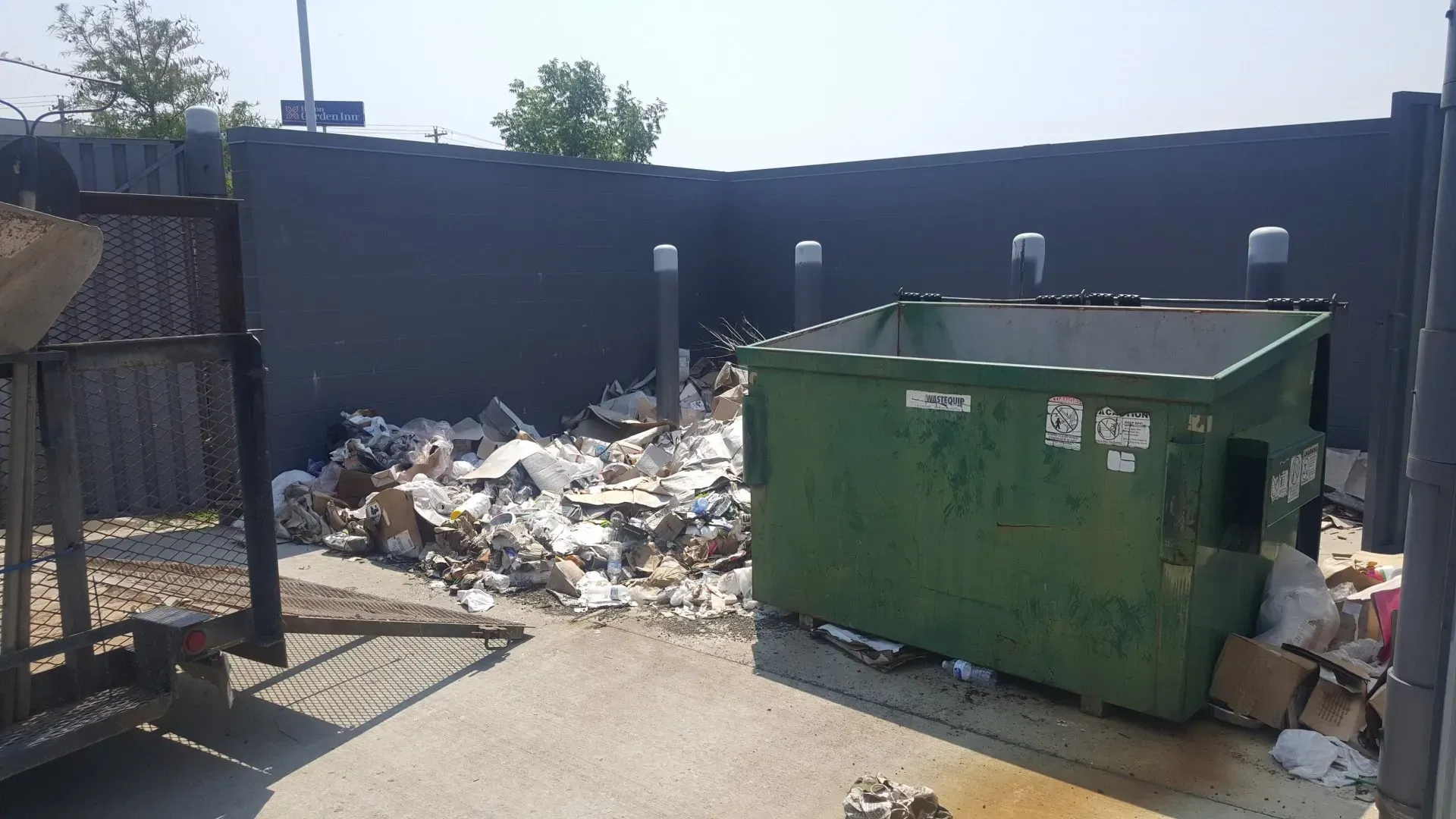 A green dumpster is sitting next to a pile of trash.