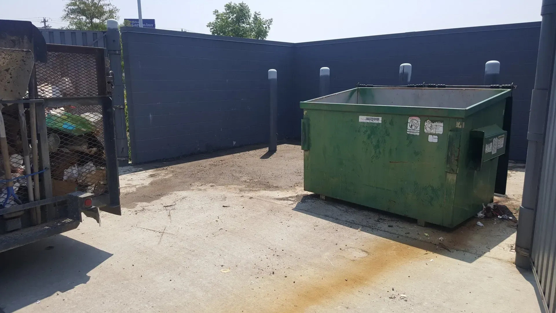 A green dumpster is sitting in a fenced in area.